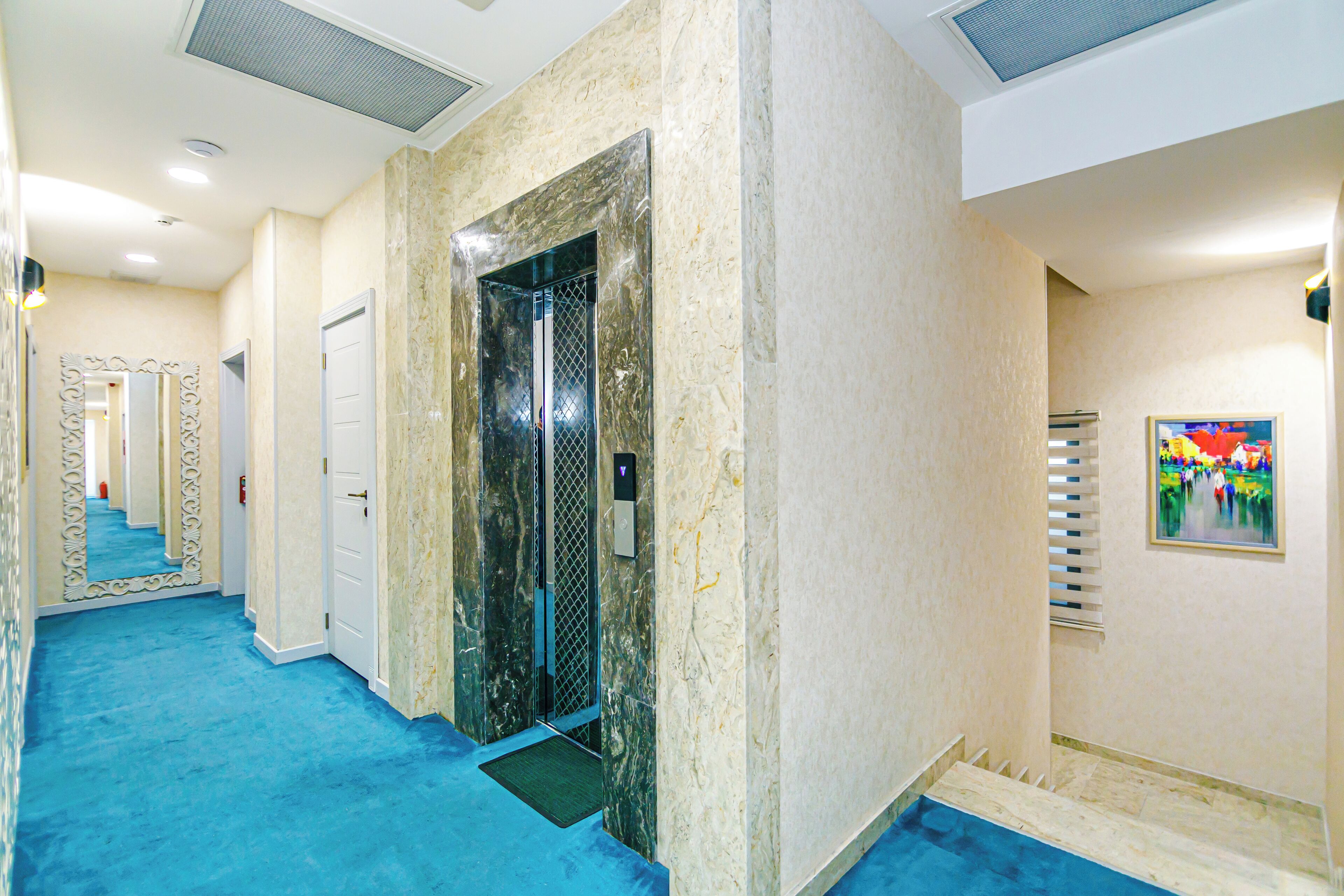 Un couloir avec un tapis bleu, une porte blanche et un mur recouvert de miroirs.