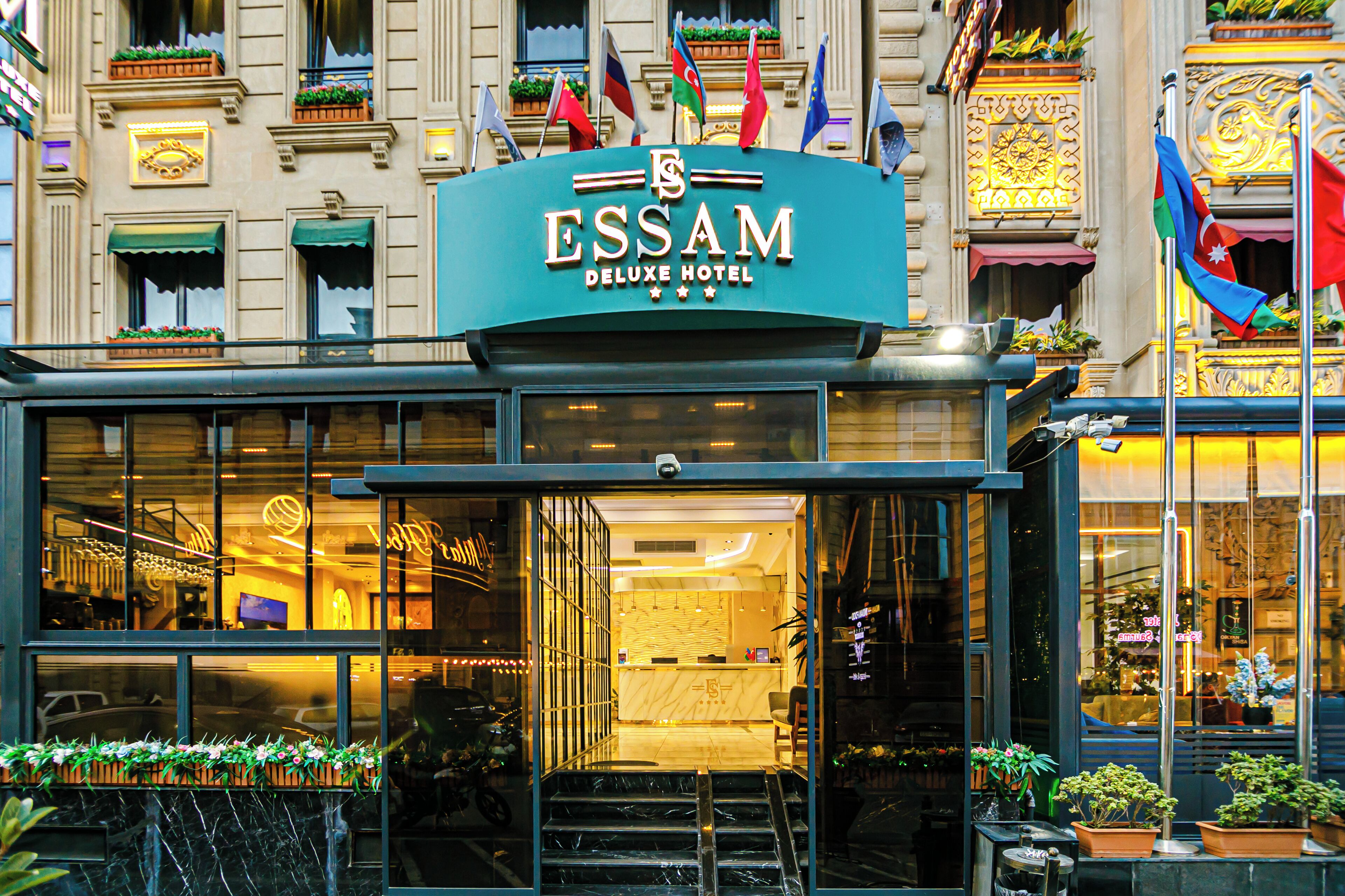 La facciata dell'ESSAM DELUXE HOTEL, con vetro, una reception e diverse bandiere.