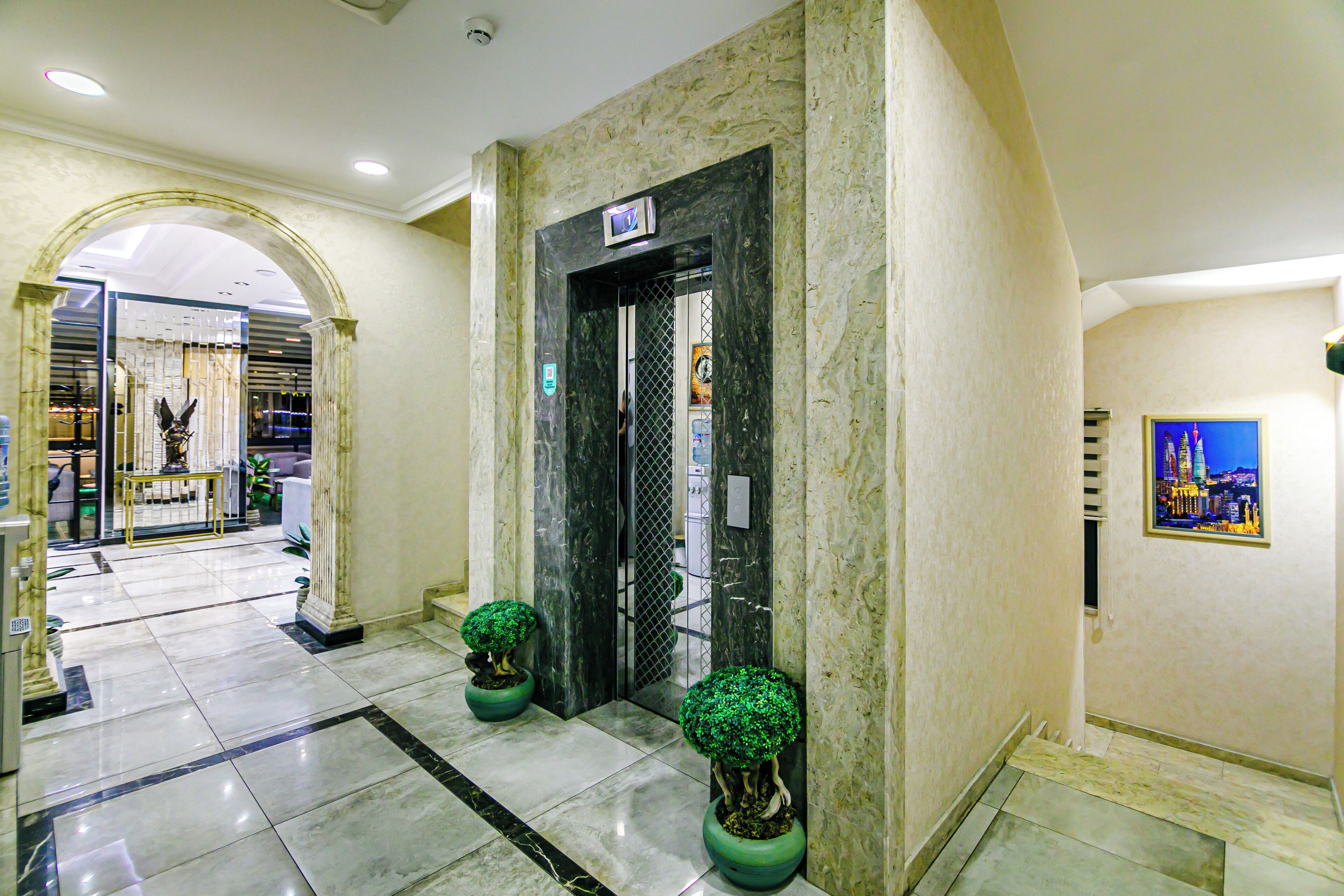 A lobby with marble flooring, a reception desk, and two potted trees.