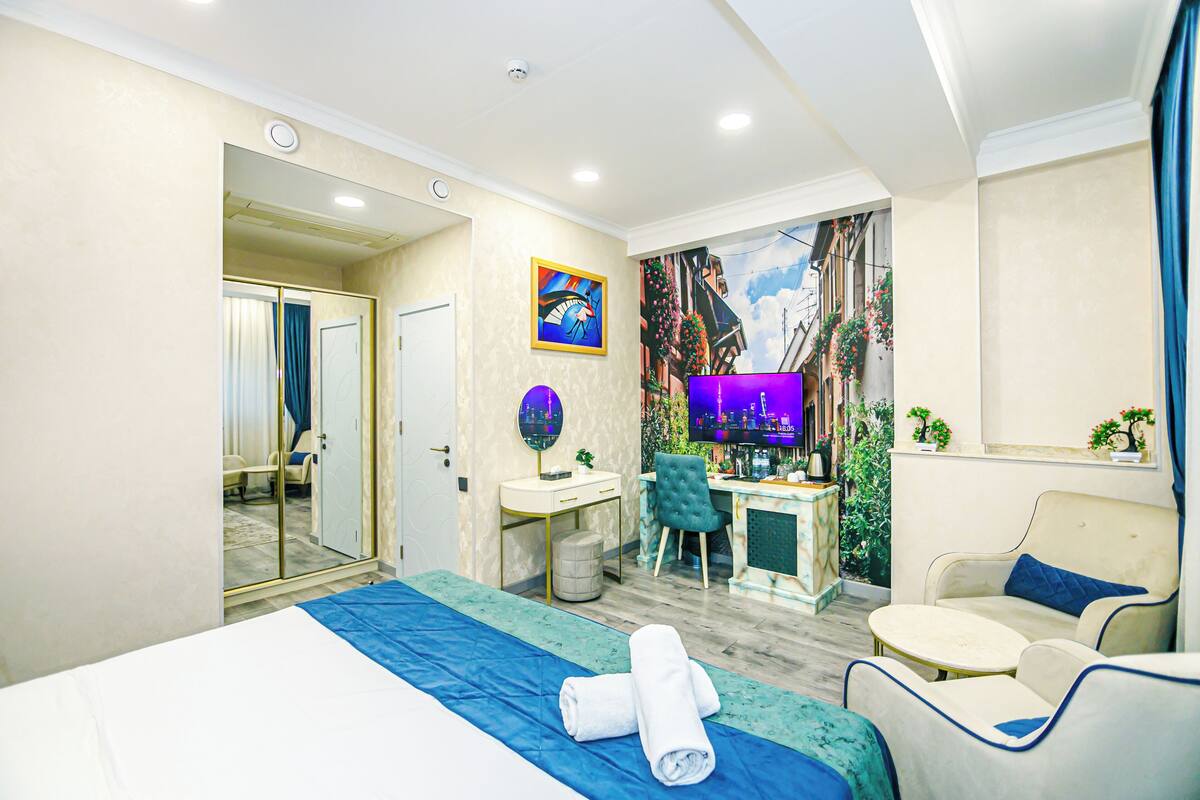A hotel room with a bed, a desk, a chair, a TV, and a sofa.