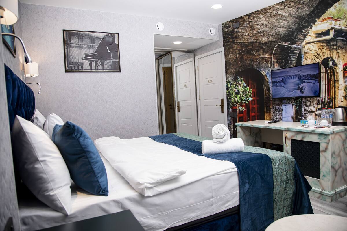 A hotel room with a bed, a desk with a computer, a TV, and a mural on the wall.
