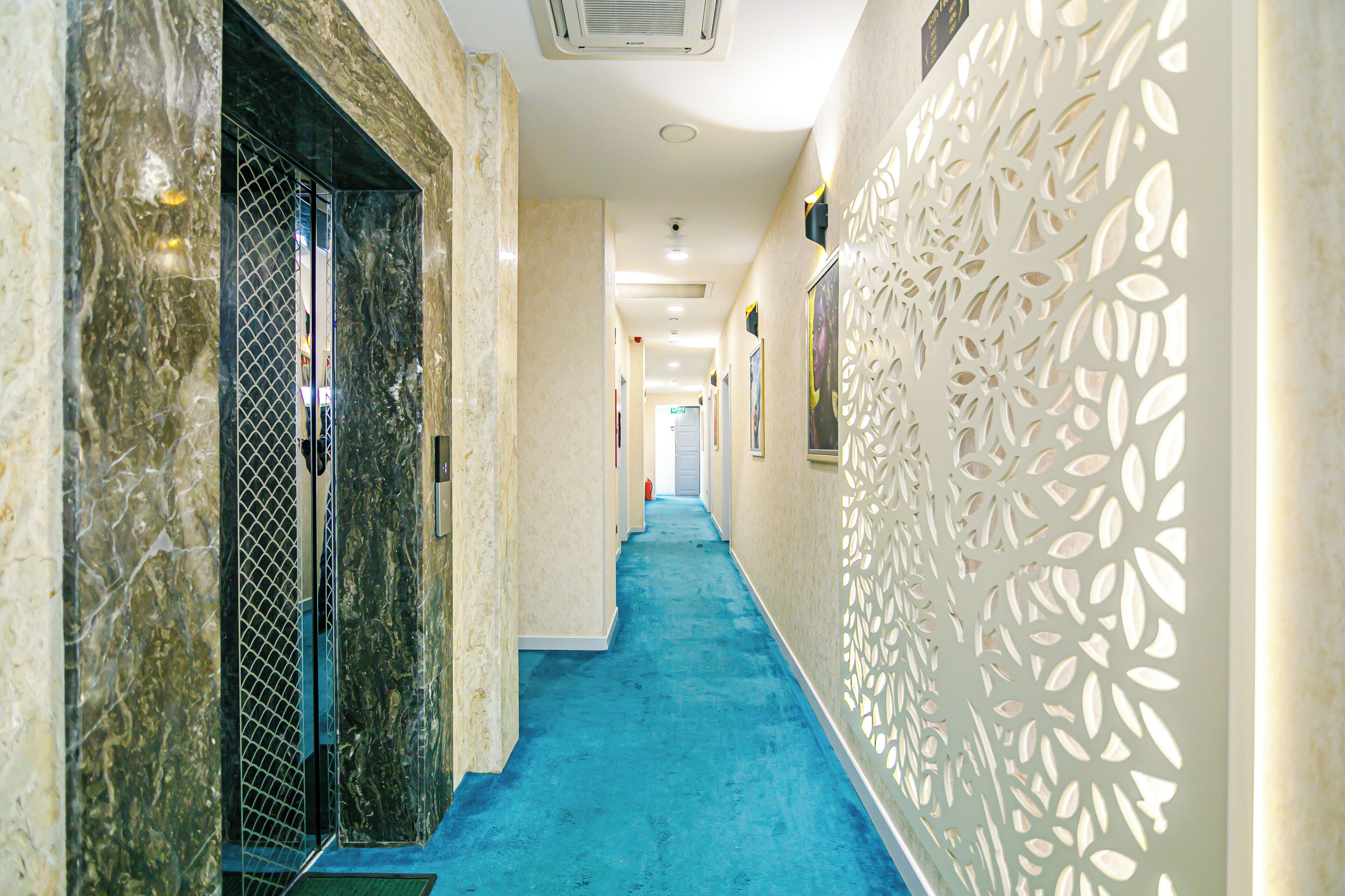 Um corredor com carpete azul, paredes de mármore e um painel branco decorativo.