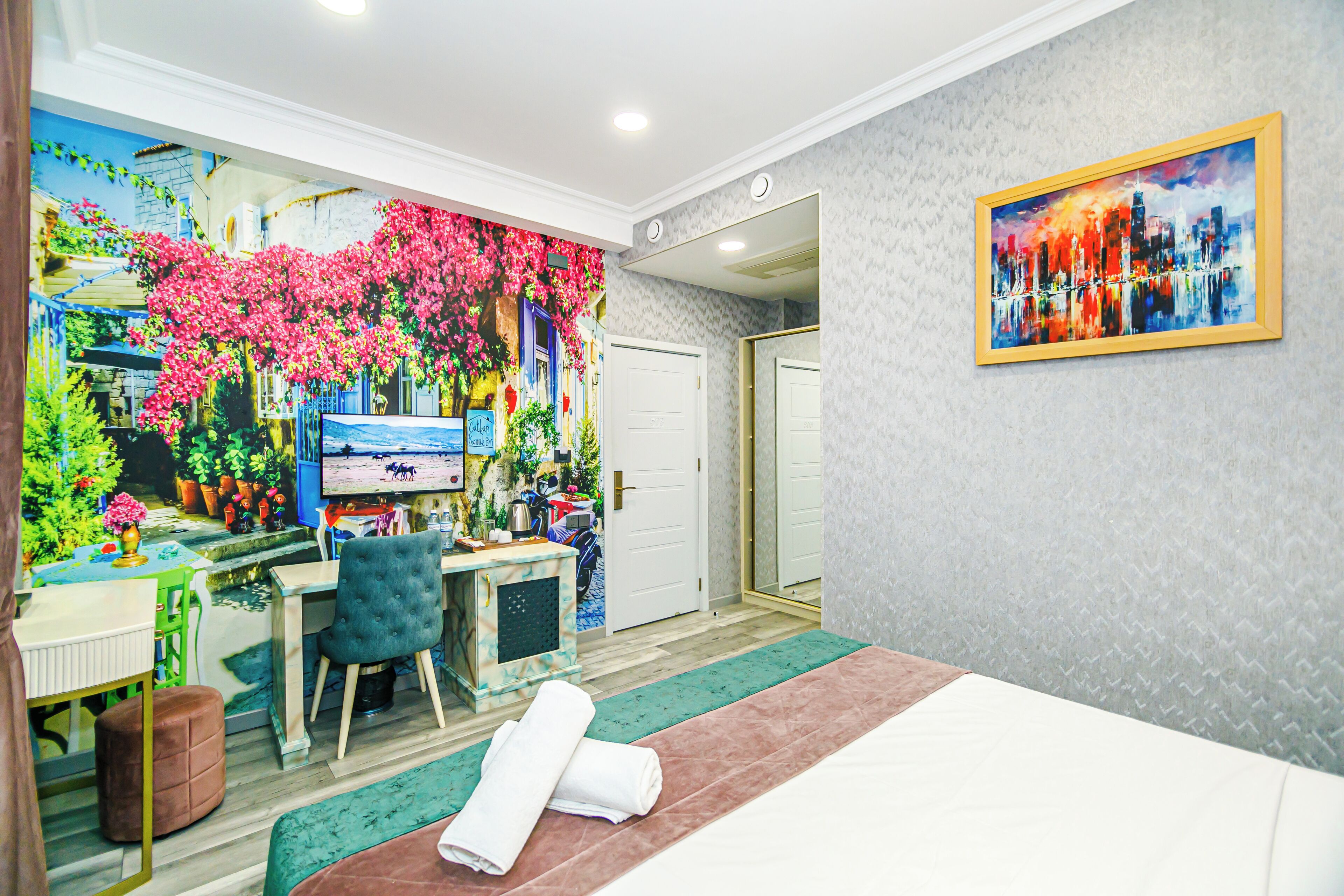 A room with a bed, a desk, a chair, a mirror, and a painting on the wall.