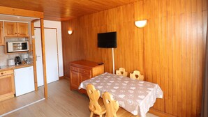 Una stanza con pannelli in legno, un tavolo da pranzo, sedie, una televisione e un angolo cottura.