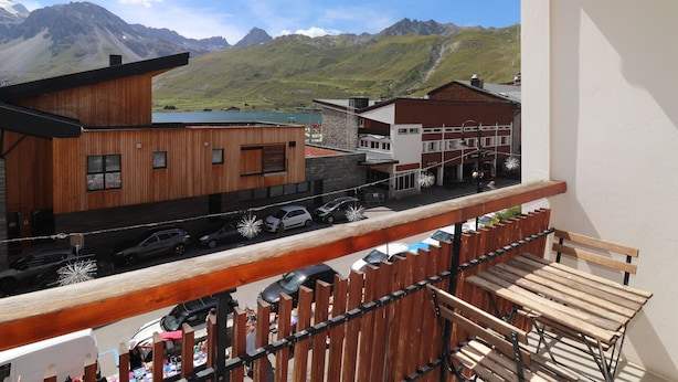 Un balcone con ringhiera in legno che si affaccia su una strada con auto e palazzi, con montagne sullo sfondo.