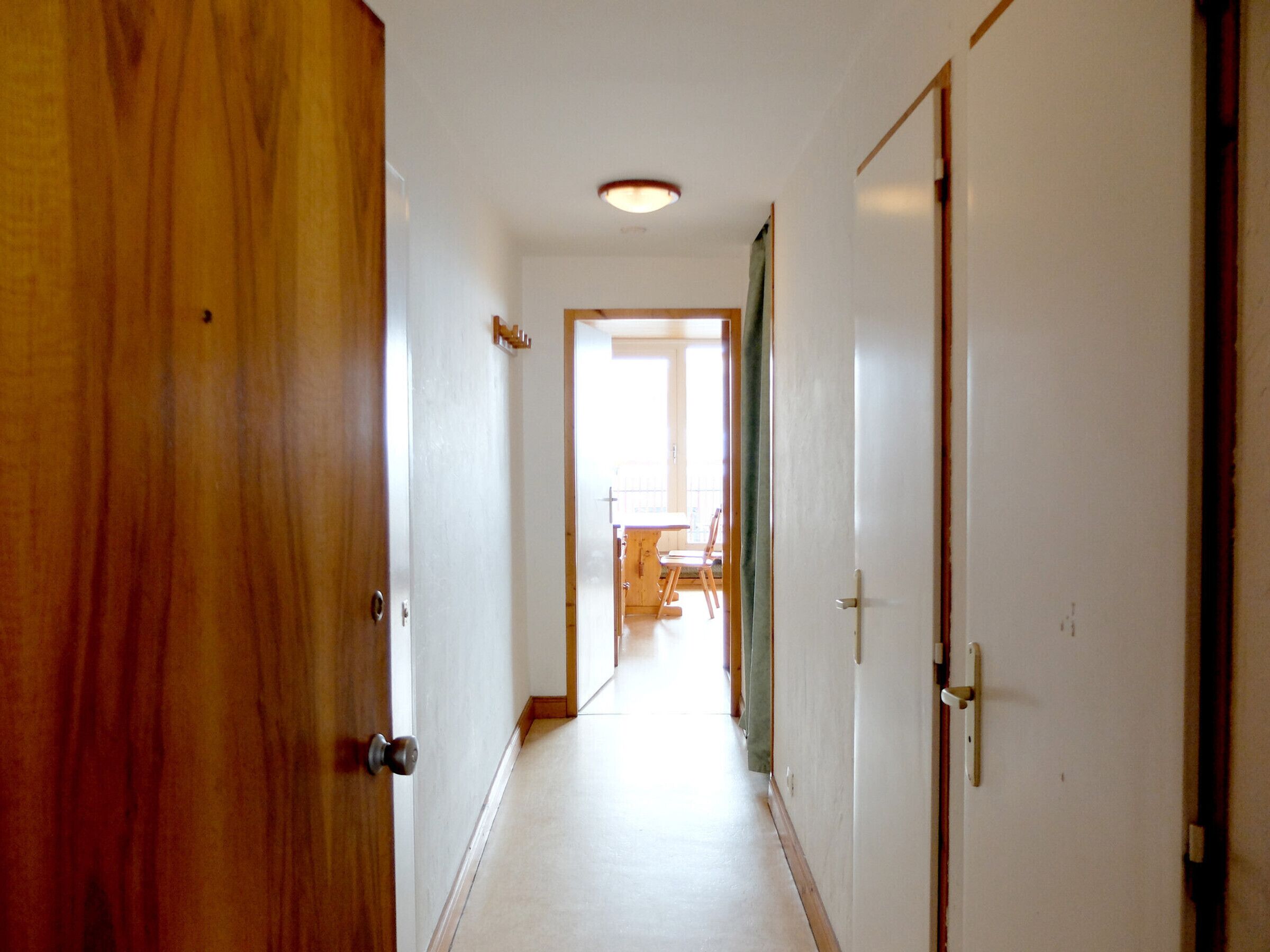 A hallway with wooden doors, a white ceiling, and a view into a room with a table and chairs.