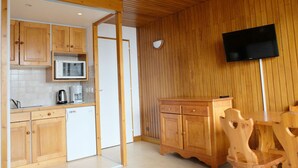 Una cucina con mobili in legno, un forno a microonde e una macchina del caffè. C'è un tavolo da pranzo in legno con sedie e un televisore montato a parete.