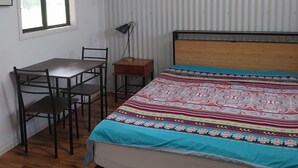 Quarto com cama, escrivaninha, cadeiras, ventoinha no teto e janela.