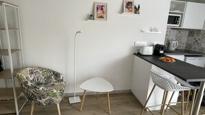 Moderni keittiö, jossa on valkoiset kaapit, mikroaaltouuni, leivänpaahdin ja hedelmäkulho työtasolla. Keittiössä on valkoinen tuoli, jossa on lehtikuvio, sekä valkoinen jakkara.