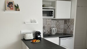 Pieni, käytännöllinen keittiö, jossa on tumma työtaso, valkoiset tuolit ja mikroaaltouuni.