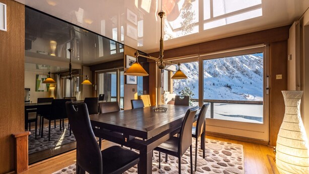 Un espace de restauration moderne, doté d’une grande table, de chaises et offrant une vue sur un paysage montagneux enneigé grâce à de larges fenêtres.