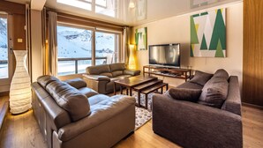 Un salon moderne avec des canapés en cuir, un téléviseur à écran plat et de grandes fenêtres offrant une vue imprenable sur les montagnes enneigées.