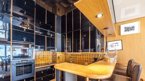 Une cuisine moderne avec des meubles noirs, un plan de travail en bois et un coin bar équipé d’un tabouret.