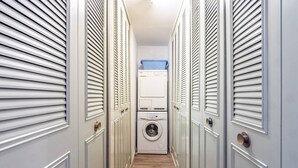 Un couloir étroit où l’on trouve une machine à laver et des paniers à linge empilés.