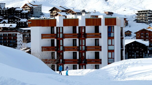 A modern building with a wooden facade, surrounded by snow-covered mountains and other buildings. - Cozy ski-in/ski-out apartment with balcony in Tignes (Tignes)