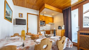 A dining area with a wooden table and chairs, a kitchen in the background, and a window with curtains. - Cozy ski-in/ski-out apartment with balcony in Tignes (Tignes)