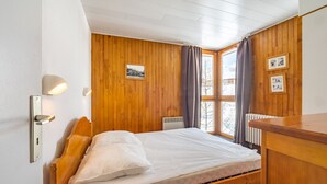 A wooden-paneled room with a bed, a radiator, and a window with curtains. - Cozy ski-in/ski-out apartment with balcony in Tignes (Tignes)