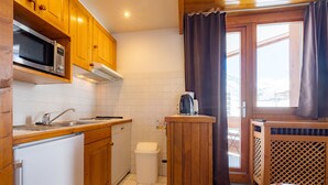 A compact kitchen with wooden cabinets, a microwave, a sink, and a small countertop. - Cozy ski-in/ski-out apartment with balcony in Tignes (Tignes)