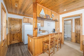 Una cucina in stile rustico con arredamento da baita, caratterizzata da mobili in legno, un'isola centrale con sgabelli da bar, un forno a microonde e un frigorifero.