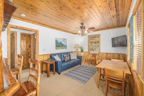 Una stanza accogliente con soffitto in legno, un divano blu, un tavolo da pranzo in legno e una TV montata a parete.