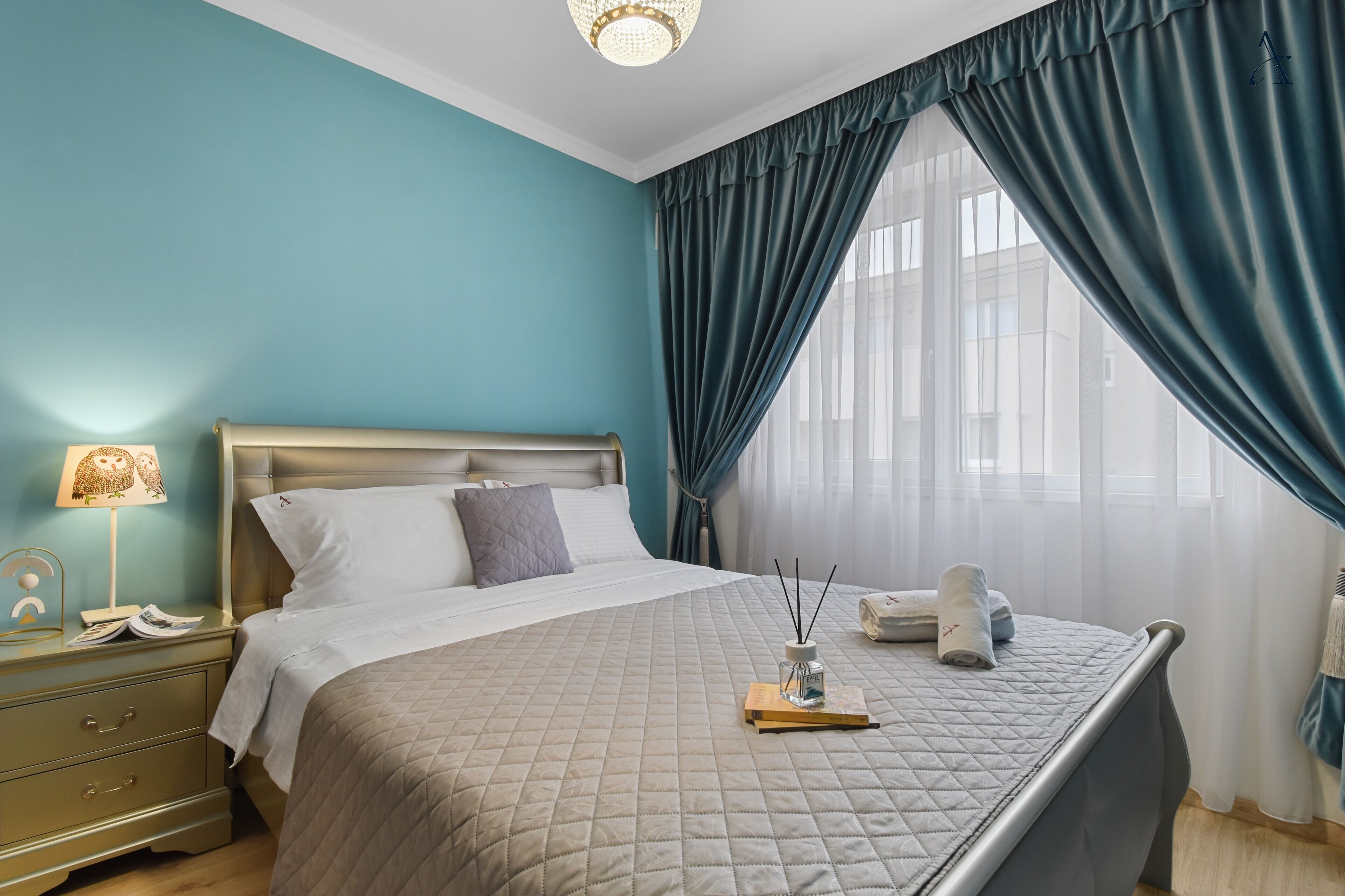 A neatly made bed with a quilted bedspread, a bedside lamp, and a nightstand with a lamp and a phone.