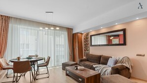 A modern living room with a sofa, ottoman, coffee table, and dining area with chairs and a table. - Sina Apartment (Voluntari)