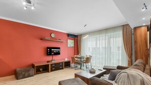 A modern living room with a red accent wall, a flat-screen TV, a dining area, and a large window with curtains. - Sina Apartment (Voluntari)