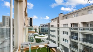 A balcony with a small table and two chairs, a grassy area, and a view of a cityscape with buildings and cars. - Sina Apartment (Voluntari)