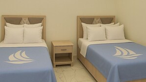 A hotel room with two beds, each with a blue bedspread and white pillows, a nightstand, and a modern ceiling design with recessed lighting.