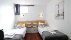 Ett hotellrum med två sängar, ett fönster med gardiner, en tavla som hänger på väggen och ett trägolv.
