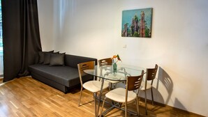 Ein modernes Wohnzimmer mit einem Esstisch mit Glasplatte, vier Stühlen, einem grauen Sofa und einem Bild an der Wand.
