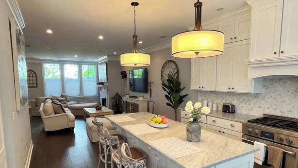 A modern kitchen with a central island, bar stools, pendant lighting, and a dining area with a sofa and chairs. - Villa De Luxe Near Forsyth Park w/Private Hot Tub (Savannah)