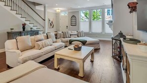 A spacious living room with a sectional sofa, a coffee table, and a staircase. - Villa De Luxe Near Forsyth Park w/Private Hot Tub (Savannah)