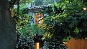 A rustic garden with a wooden fence, a stone wall, and a house with a tiled roof. - Daudet Romantic two-person apartment in Provence (St Remy de Provence Quartier de Paluds)