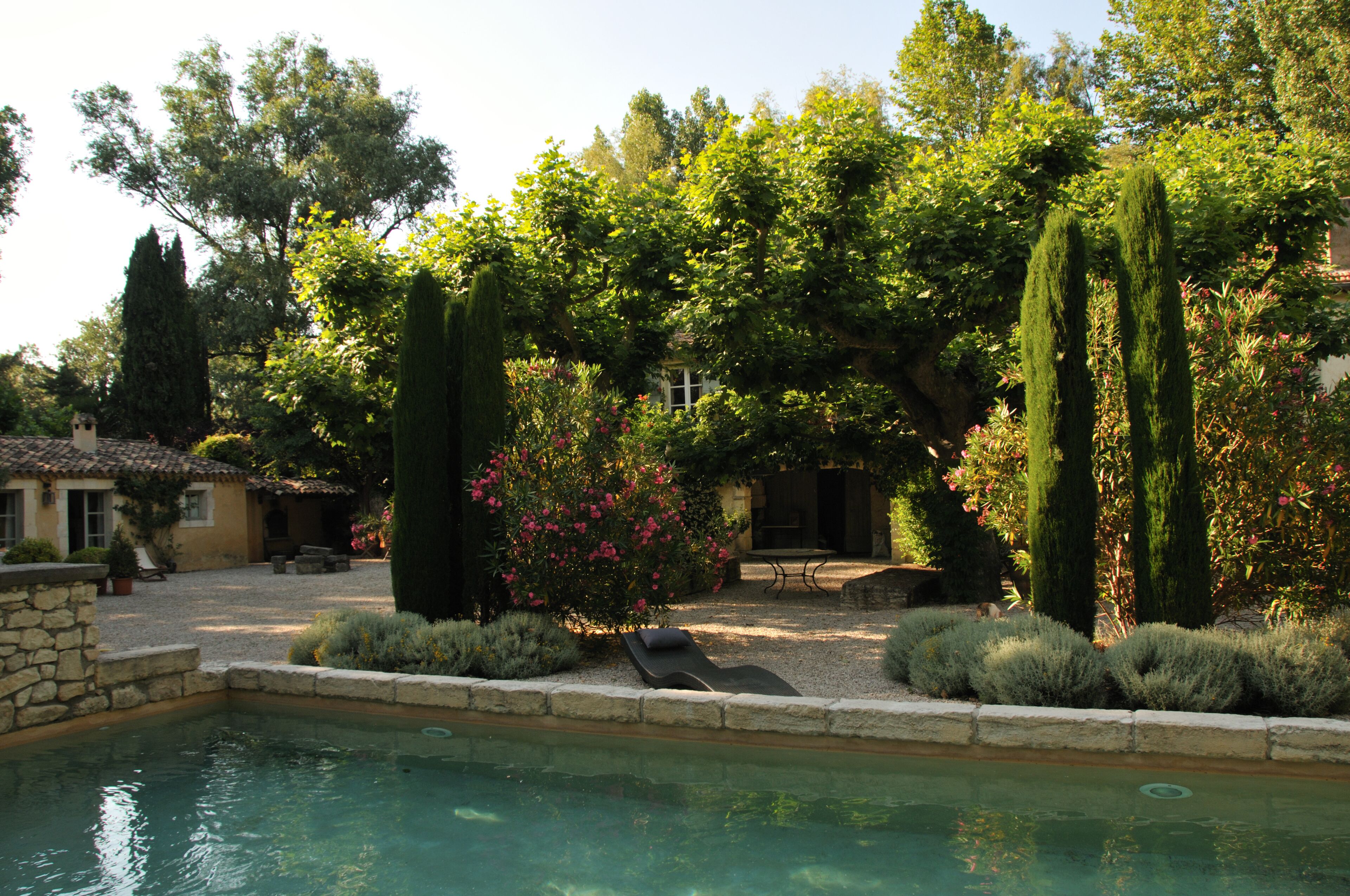 A pool area with a stone wall, a lounge chair, and a patio with a table and chairs.
