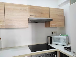 A modern kitchen with wooden cabinets, a black induction cooktop, a white microwave, and a kettle. - Lovely Modern Historical 1-bedroom (Vienna)