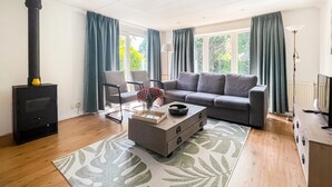 A living room with a sofa, a coffee table, a fireplace, and a view of greenery outside. - Lovely (sta)caravan in Putten with WiFi (Putten)