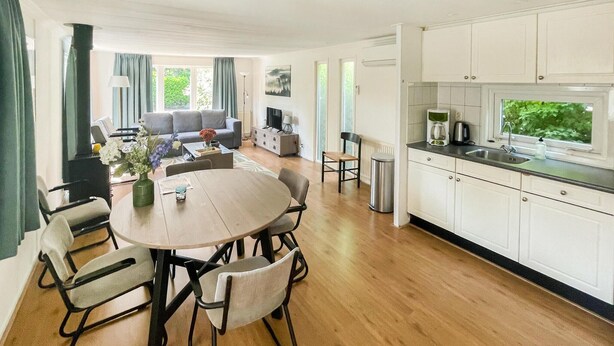 A modern kitchen with white cabinets and a black countertop, a dining area with a round table and chairs, and a living room with a grey sofa and a TV. - Lovely (sta)caravan in Putten with WiFi (Putten)