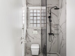 A modern bathroom with a glass-enclosed shower, a toilet, and a window with frosted glass panels. - Sanders Old Port - Cute 1-bdr. Apt. w/ Balcony (Thessaloniki)