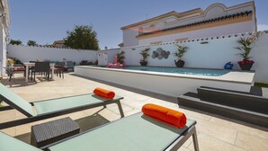 A pool area with lounge chairs and a small table, surrounded by potted plants and a white wall with decorative elements. - Spanish villa with private pool , only 5 minutes from the beach! (San Pedro de Alcantara)