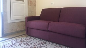 Ein violettes Sofa in einem Raum mit Fliesenboden und einer teilweise geöffneten weißen Tür.