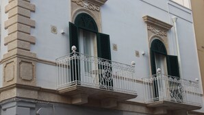 Ein Gebäude mit zwei Balkonen und aufwendig gestalteten Metallgeländern sowie grünen Fensterläden.
