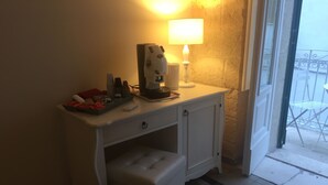 Ein kleiner, weißer Schreibtisch mit Kaffeemaschine, einer Lampe und einer Ablage mit Tassen und einer roten Box.