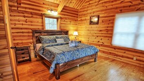 Ein Schlafzimmer in einer Holzhütte mit einem Bett, einem Nachttisch, einem Fenster und einer Wandleuchte.