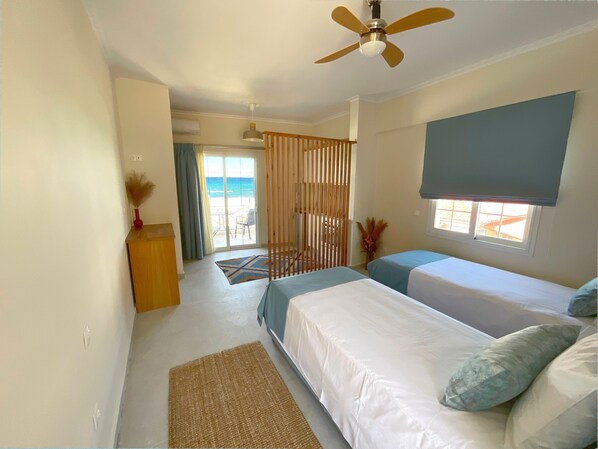 Quarto com duas camas, um ventilador de teto, janela com vista e porta para uma varanda.