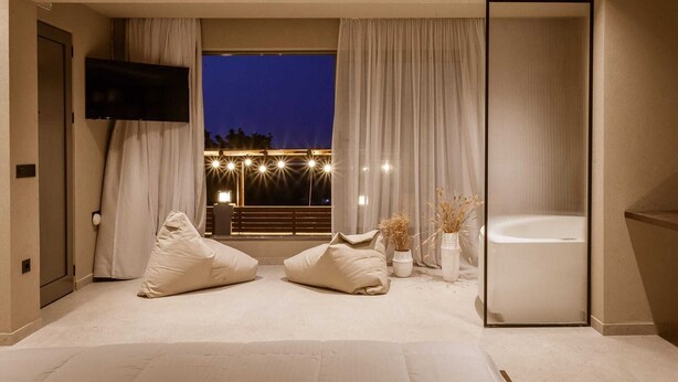A modern bedroom with a large window, a flat-screen TV, a bathtub, and two bean bags. - Sevasti Seaview Suite (Rhodes)
