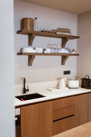 A modern kitchen with wooden cabinets, a white countertop, a built-in sink, and a shelf above holding dishes and glassware.