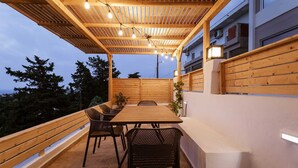 An outdoor patio with a wooden table and chairs, a pergola with string lights, and a view of a building in the background. - Sevasti Seaview Suite (Rhodes)
