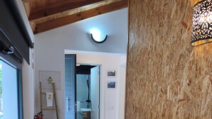 Een trap met houten treden en een metalen leuning, die leidt naar een kamer met een houten plafond en een wandlamp.