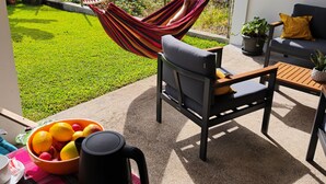 Een terras met een hangmat, zitplaatsen en een tafel met fruit en een koffiepot.